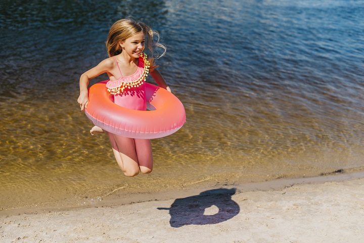 Девочка с надувным кругом прыгает у морского берега 