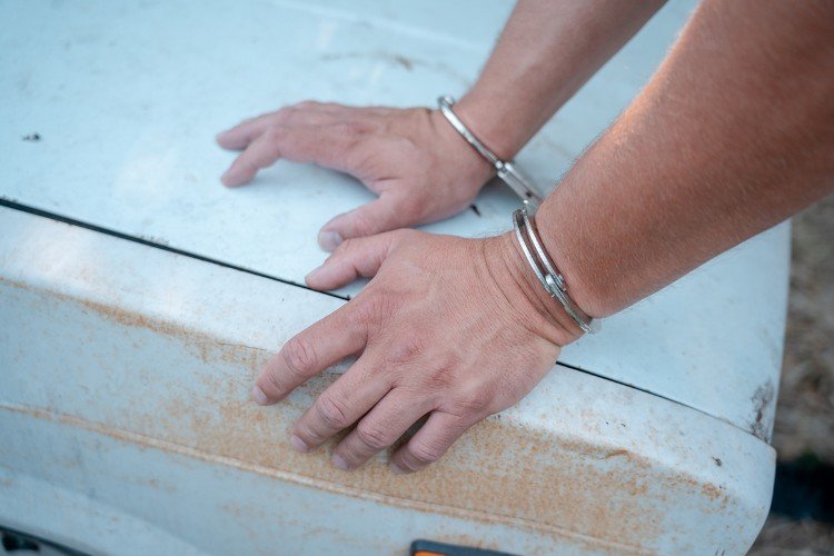 руки в наручниках упираются в капот авто