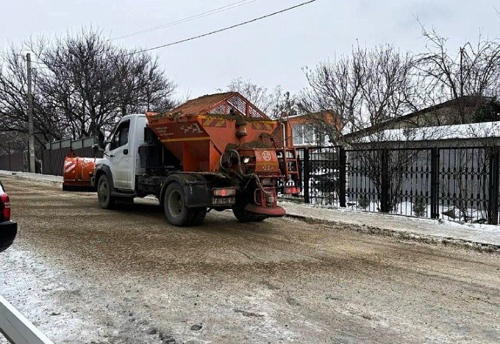 машина посыпает песком дорогу