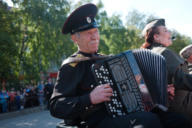 Старик в казачьей форме играет на гармошке