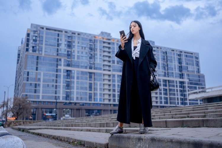Девушка смотрит в телефон на фоне новостройки в Краснодаре
