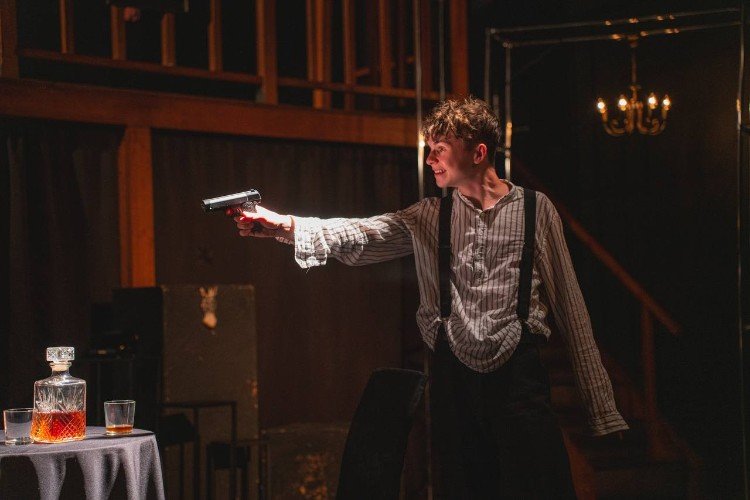 Юноша целится из пистолета на сцене театра