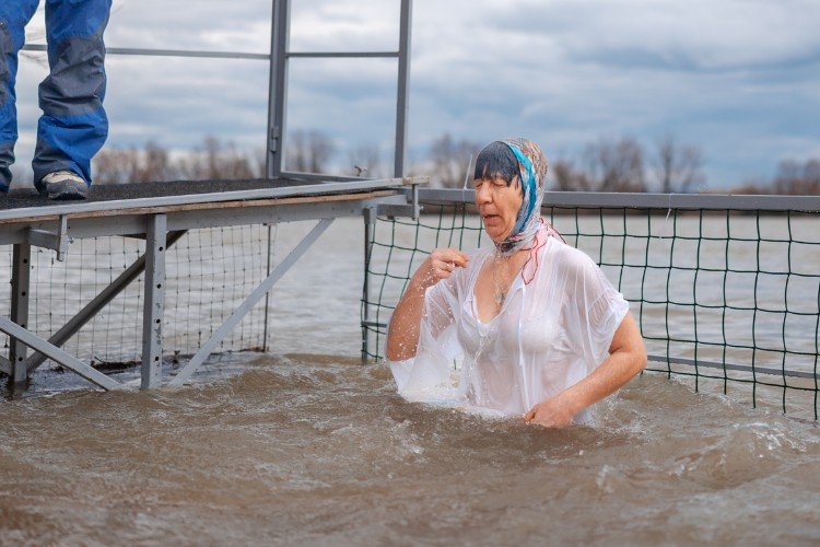 Женщина крестится в мутной воде