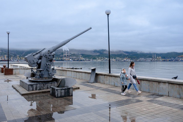 Люди идут около пушки на набережной