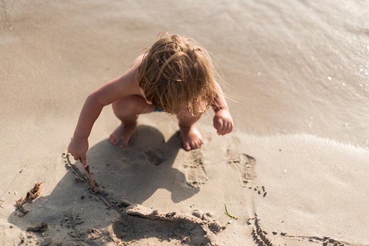 Раздетый маленький ребенок сидит на песке у моря