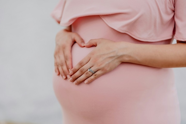 Беременная женщина в розовом платье держит руки на животе