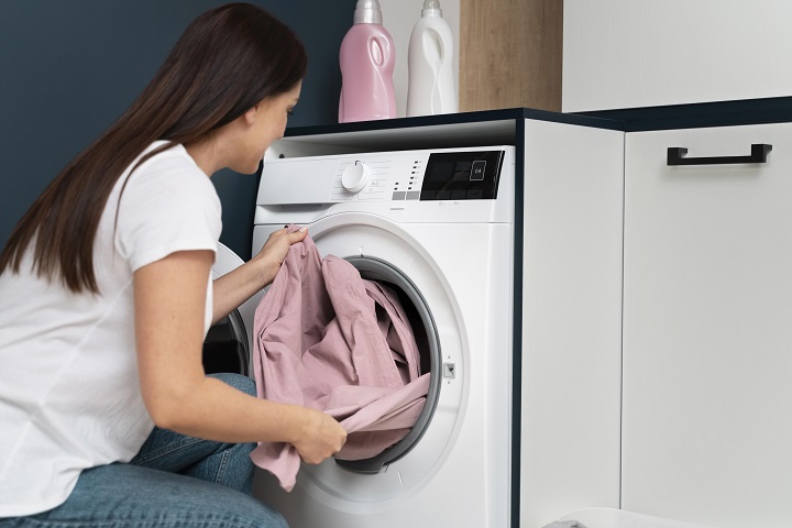 Женщина вытаскивает выстиранное белье из стиральной машины