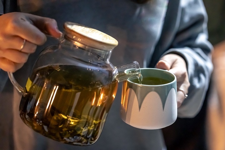 Женщина наливает из чайника в кружку зеленый чай
