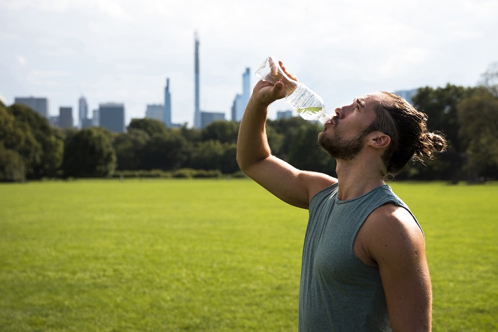 Молодой мужчина спортивного телосложения пьет воду из бутылочки
