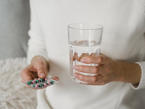 Женщина держит в руках блистер с таблетками и стакан воды