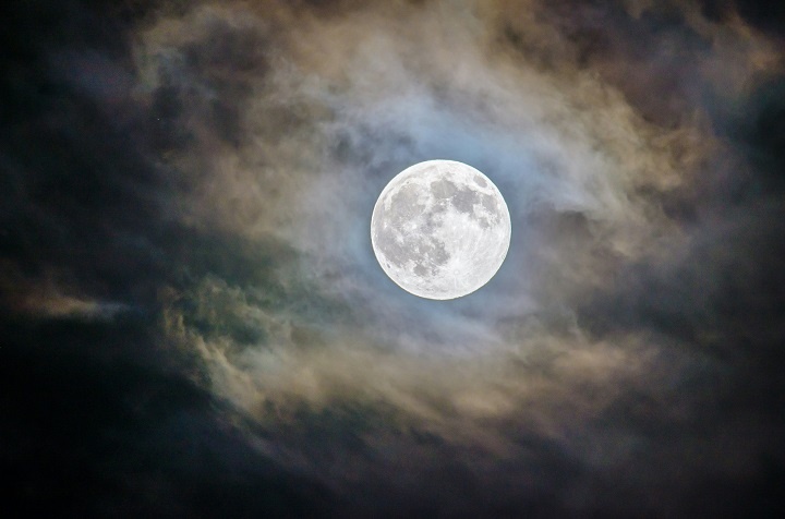 Полная луна в ночном небе проглядывает сквозь тучи