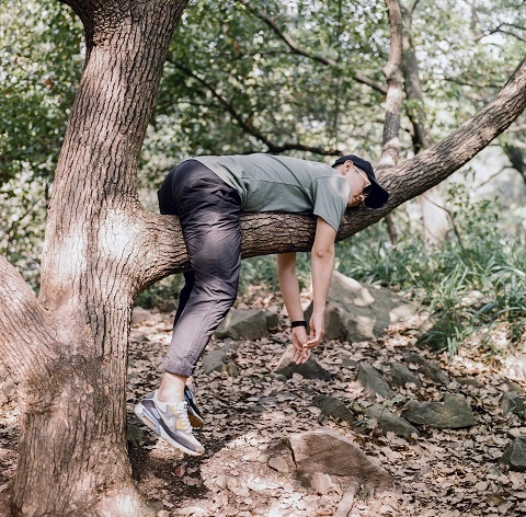Молодой человек лежит на ветке дерева в позе ленивца 