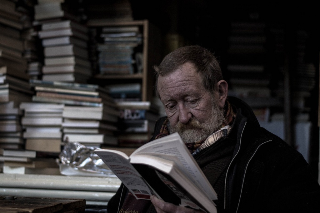 Пожилой мужчина читает печатную книгу в книжной лавке