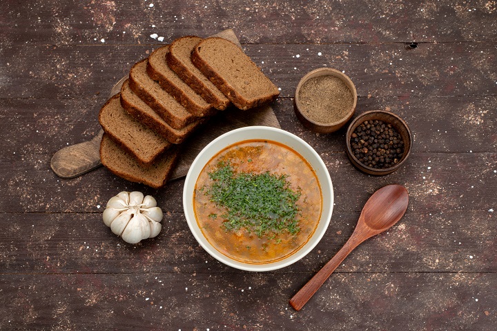 Овощной суп с черным хлебом и головой чеснока на сером фоне 