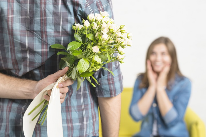 Молодой человек держит за спиной в левой руке букет цветов для любимой девушки