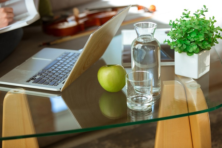 Графин с водой, стакан и зеленое яблоко стоят на столике у ноутбука