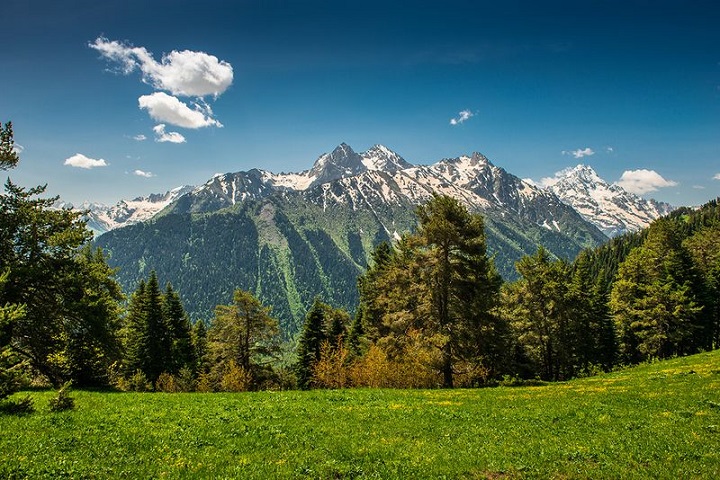 Зеленый луг среди заснеженных гор 