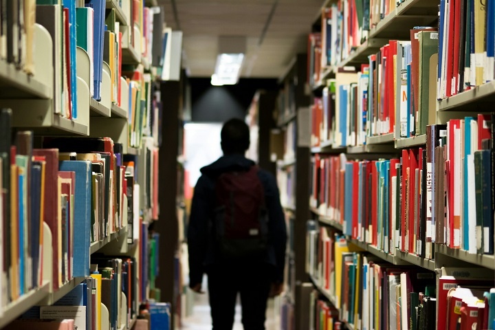 Мужчина стоит в библиотеке среди полок с книгами 