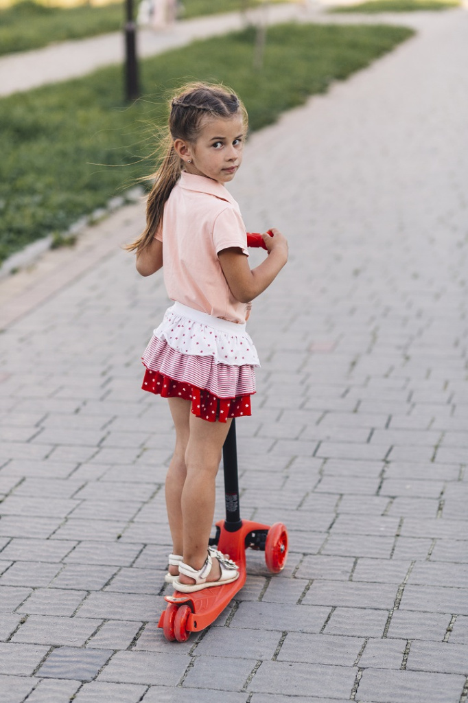 Девочка стоит на самокате, обутая в белые сандалии
