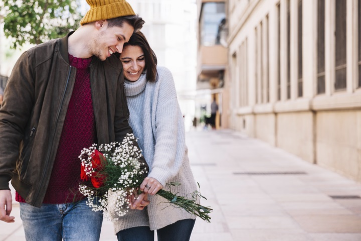 Молодой человек и девушка с букетом роз гуляют по улице