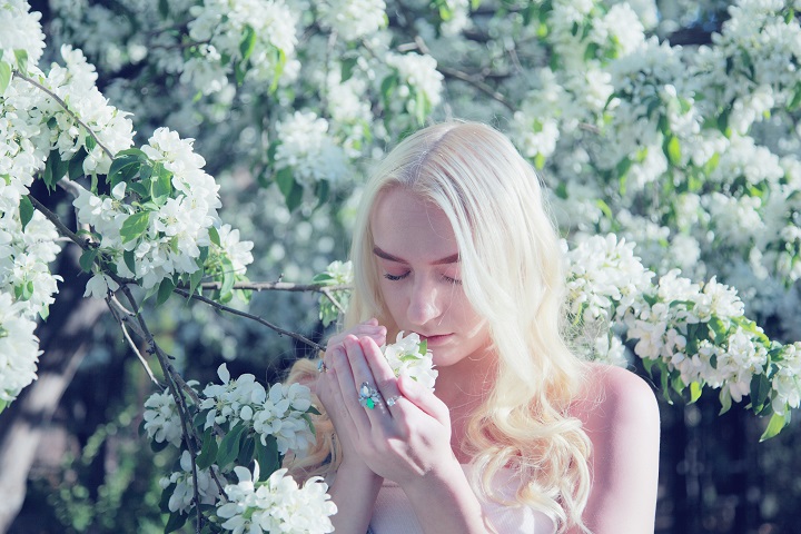Молодая белокурая девушка вдыхает аромат цветущего дерева