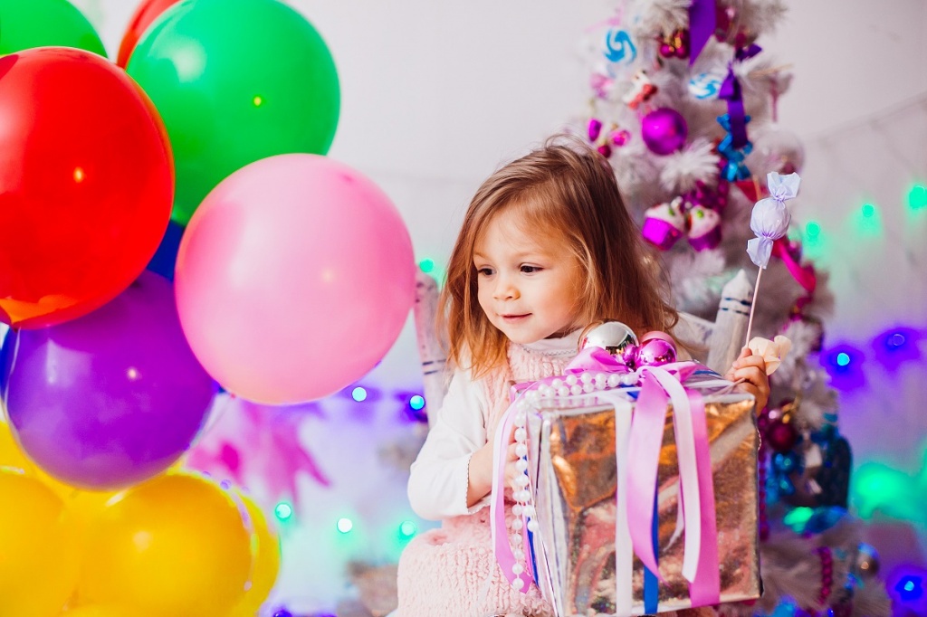 Маленькая девочка у новогодней елки с подарками 