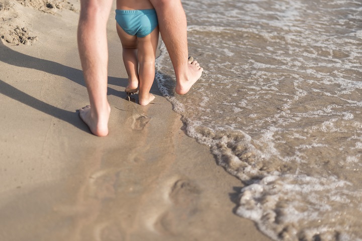 Папа водит малыша босиком по пляжному песку 