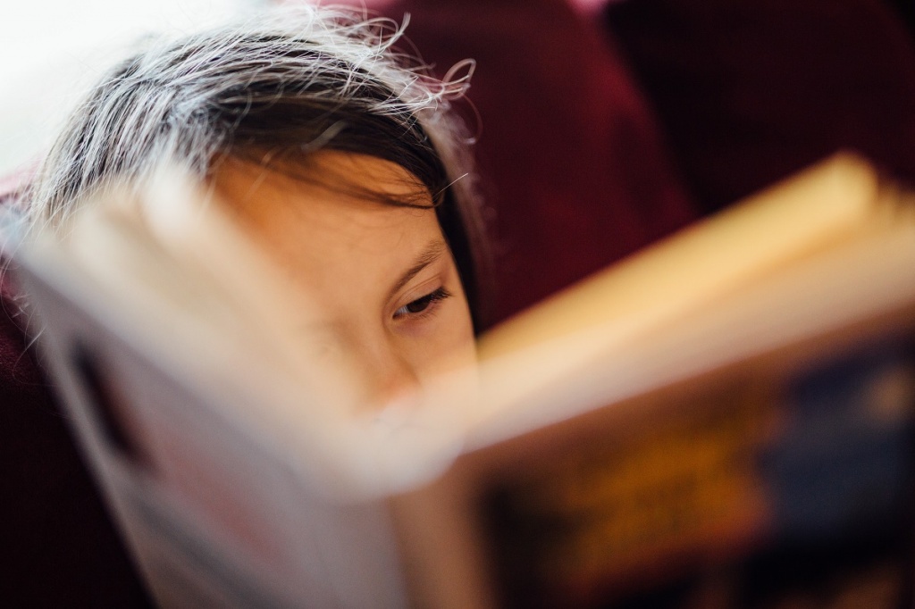 Маленькая девочка читает бумажную книгу
