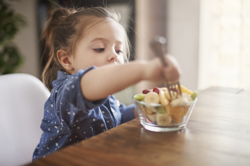 Маленькая девочка ест нарезанные фрукты