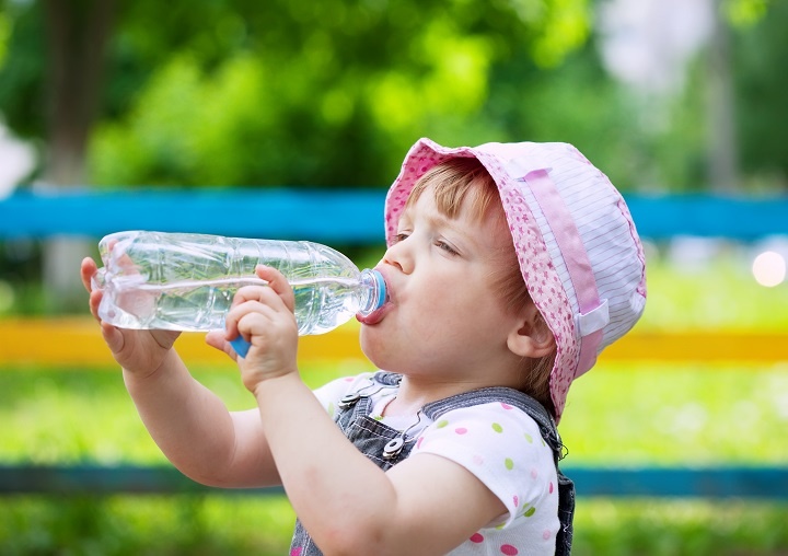 Двухлетняя девочка пьет воду из бутылки на прогулке