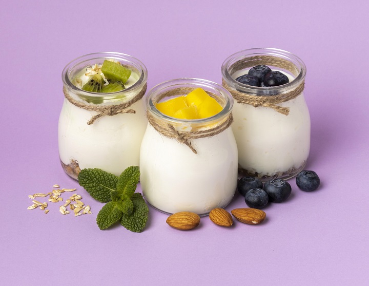 Три баночки с натуральным йогуртом и фруктами на сиреневом фоне 