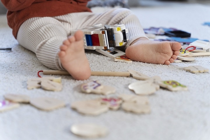 Маленький ребенок с босыми ногами сидит на ковре и играет с машинкой