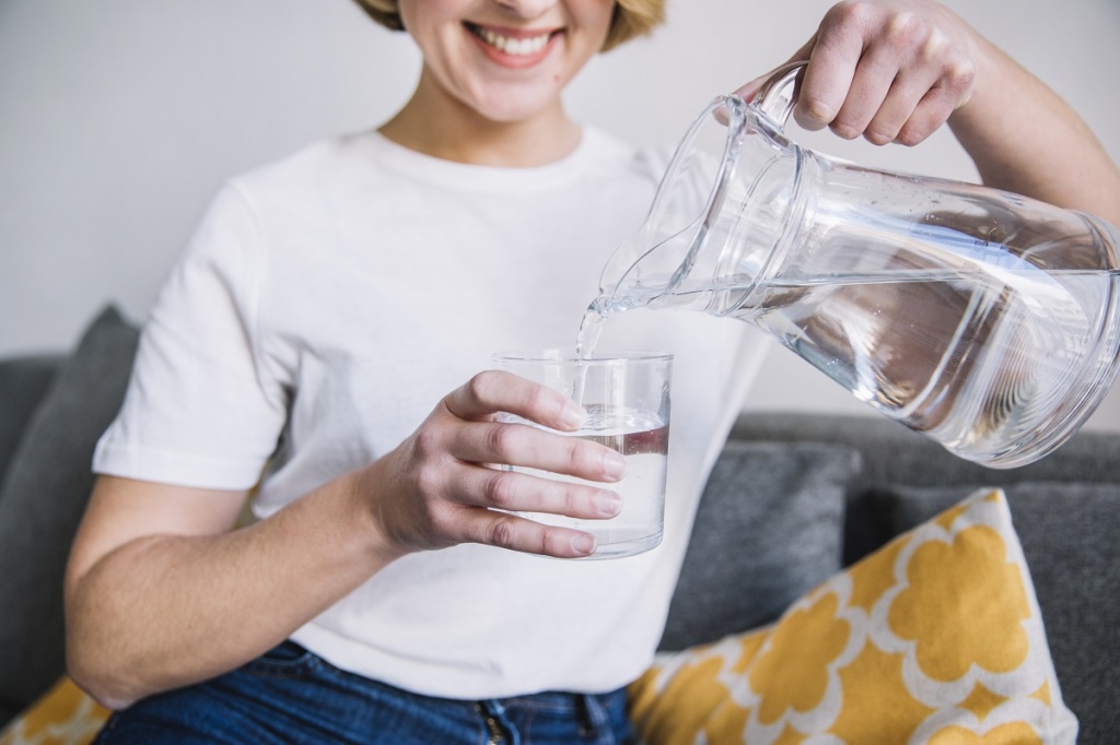 Молодая девушка наливает себе воду из кувшина