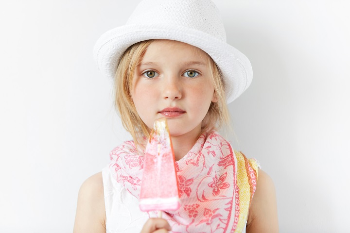 Маленькая девочка в белой панамке на голове ест фруктовое мороженое