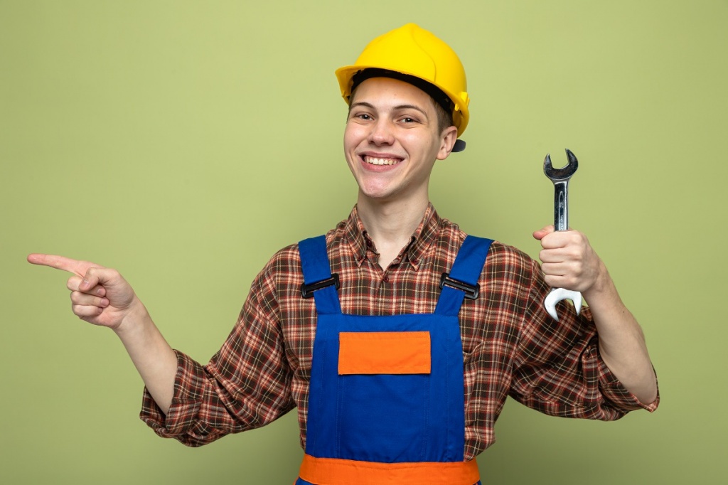 smiling-points-side-young-male-builder-wearing-uniform-holding-open-end-wrench.jpg