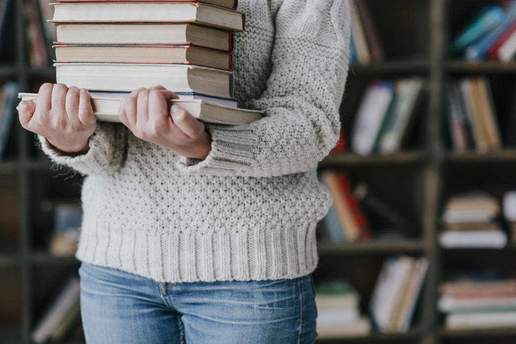 Женщина несет стопку книг