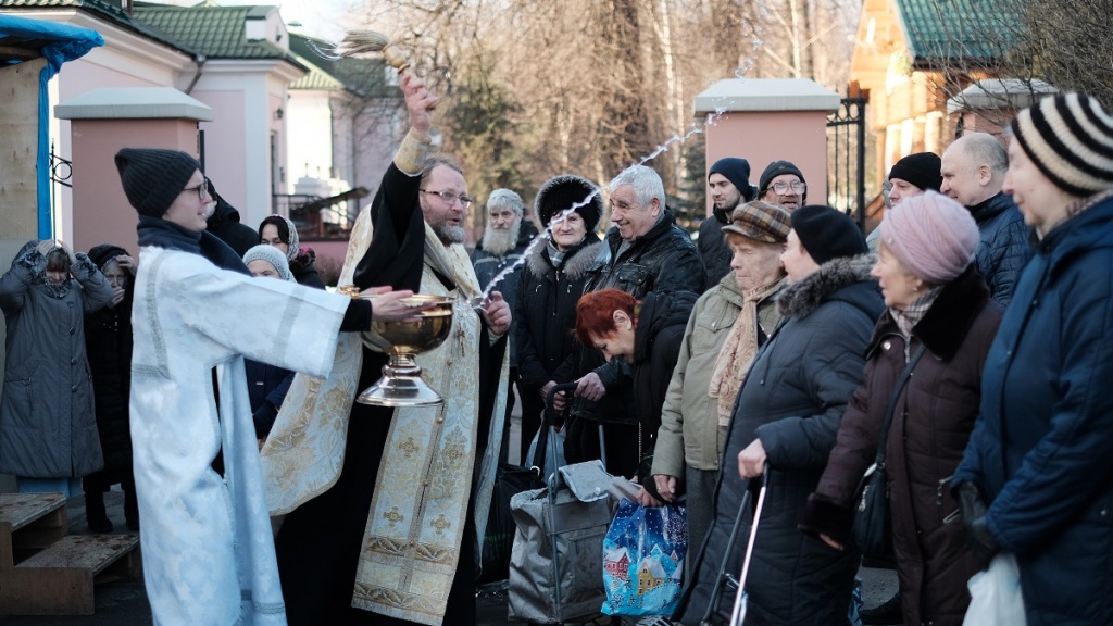 Служитель церкви освещает воду на Крещение 