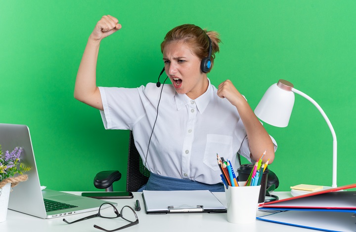 confident-young-blonde-call-centre-girl-wearing-headset-sitting-desk-with-work-tools-looking-laptop-doing-strong-gesture-isolated-green-wall_2.jpg Молодая женщина полна энергии сидит за рабочим столом