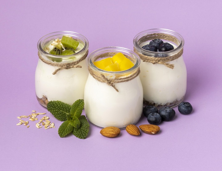 composition-delicious-breakfast-meal-with-yogurt.jpg Три баночки с натуральным йогуртом и фруктами на сиреневом фоне