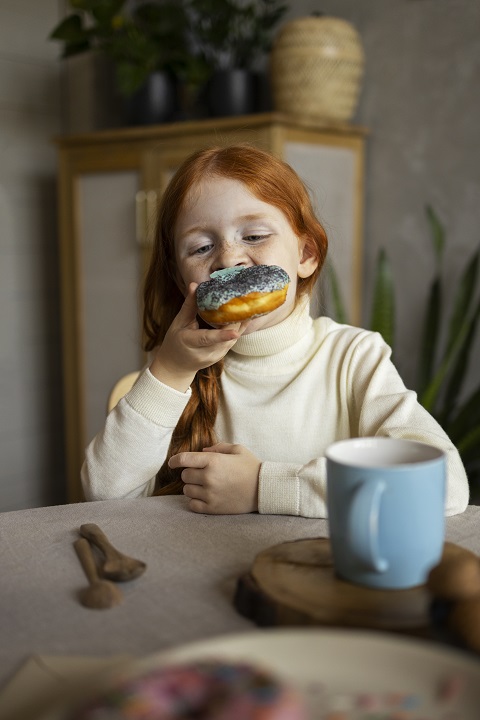 child-doing-household-activities-indoors.jpg Девочка за столом ест пончик с глазурью