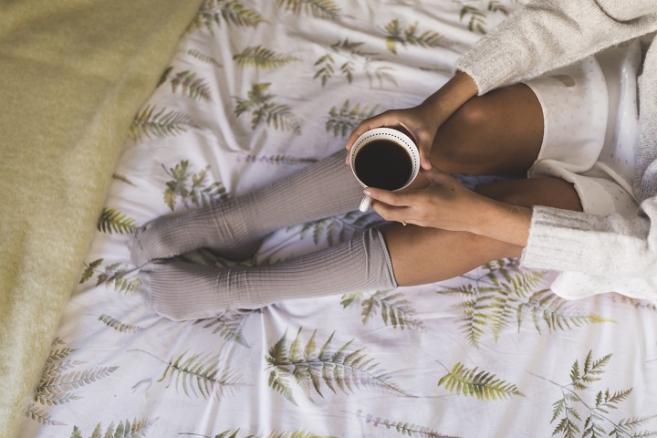 top-view-teenage-girl-sitting-bed-holding-coffee-cup.jpg Девушка в серых гольфах сидит на кровати с чашкой кофе